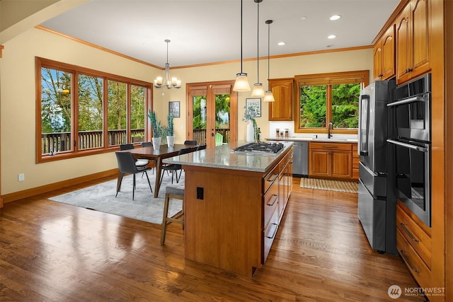 kitchen with a sink, a kitchen island, wood finished floors, stainless steel appliances, and brown cabinetry