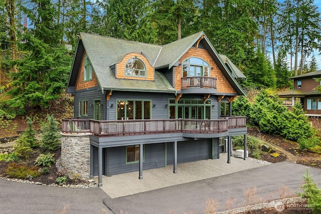 view of front facade with aphalt driveway, a balcony, roof with shingles, and a garage