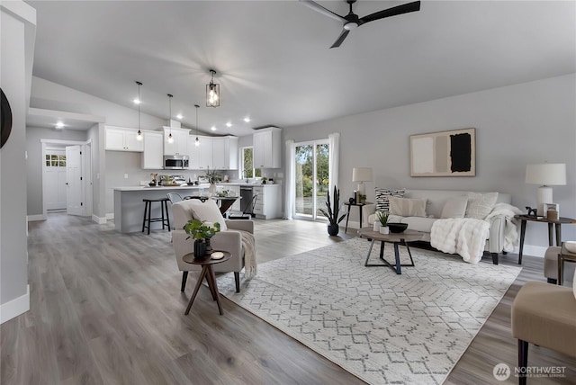 living area with baseboards, light wood-style flooring, a ceiling fan, and lofted ceiling