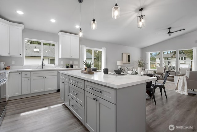 kitchen with a sink, a kitchen island, open floor plan, light wood finished floors, and vaulted ceiling