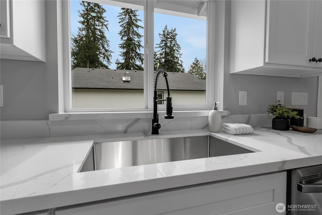 interior details featuring white cabinets, light stone countertops, and a sink