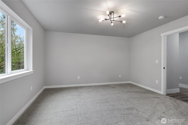 carpeted spare room with baseboards and a chandelier