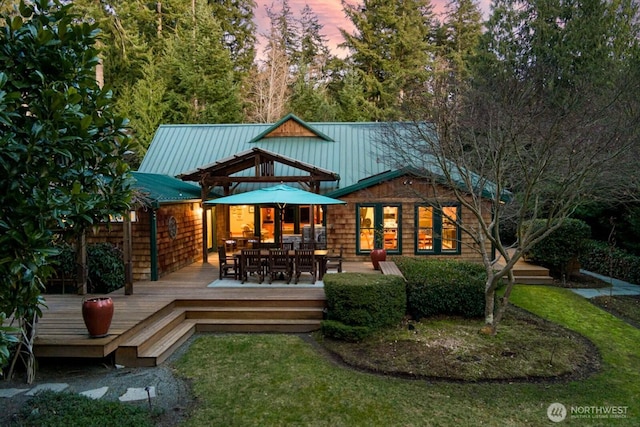 rear view of house with a yard, metal roof, outdoor dining area, and a deck