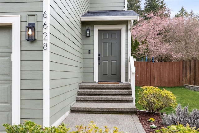 entrance to property featuring fence, a garage, and roof with shingles