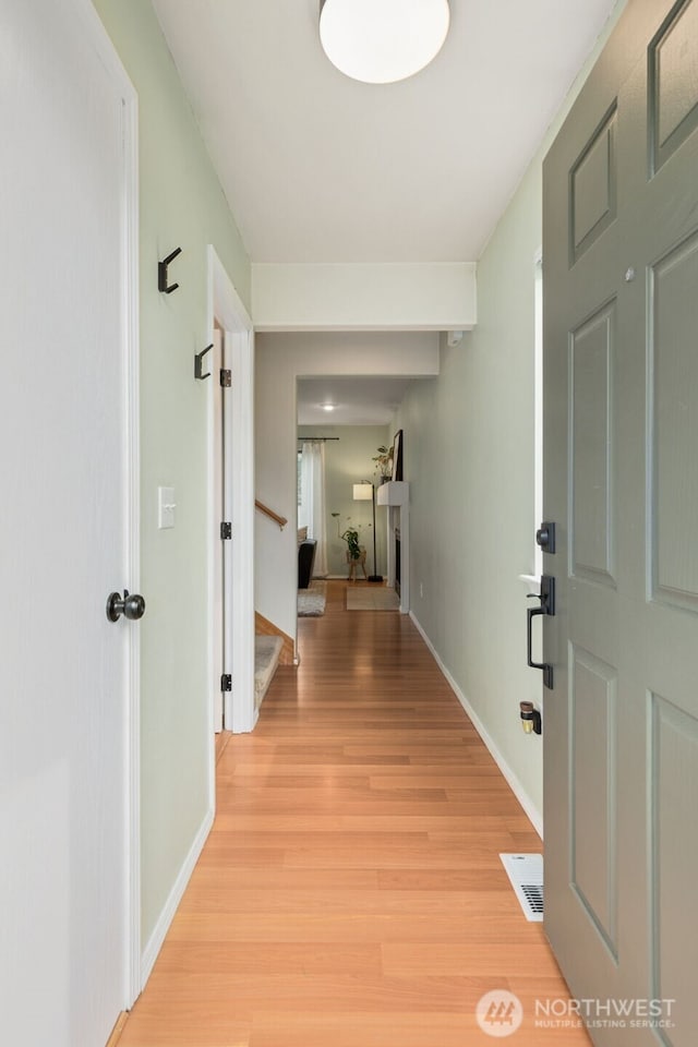 hall with visible vents, baseboards, light wood-style floors, and stairs