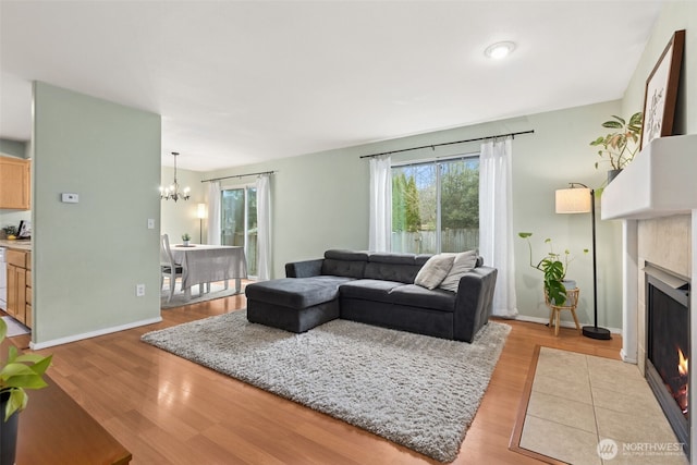 living area with a chandelier, a fireplace with flush hearth, baseboards, and light wood-style flooring