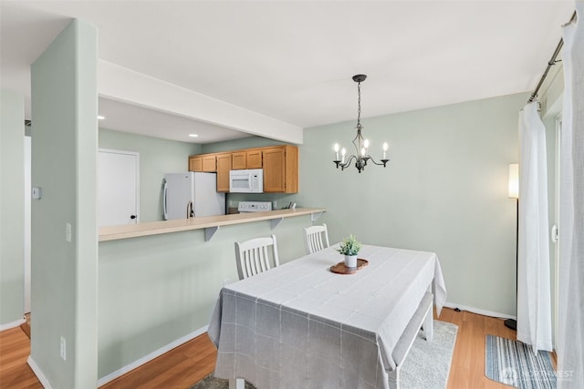 dining space with baseboards, an inviting chandelier, and light wood-style flooring