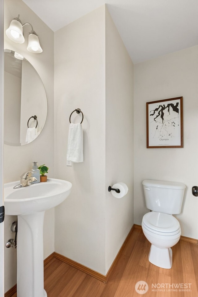 half bath with toilet, wood finished floors, baseboards, and a sink