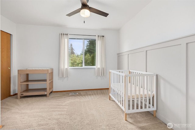 carpeted bedroom with baseboards, visible vents, a crib, and ceiling fan