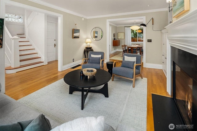 living room with a fireplace with flush hearth, stairs, crown molding, and wood finished floors