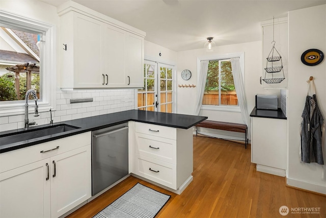 kitchen featuring a peninsula, light wood-style flooring, a sink, dishwasher, and dark countertops