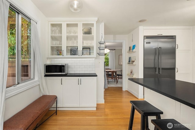 kitchen with glass insert cabinets, appliances with stainless steel finishes, white cabinetry, dark countertops, and tasteful backsplash