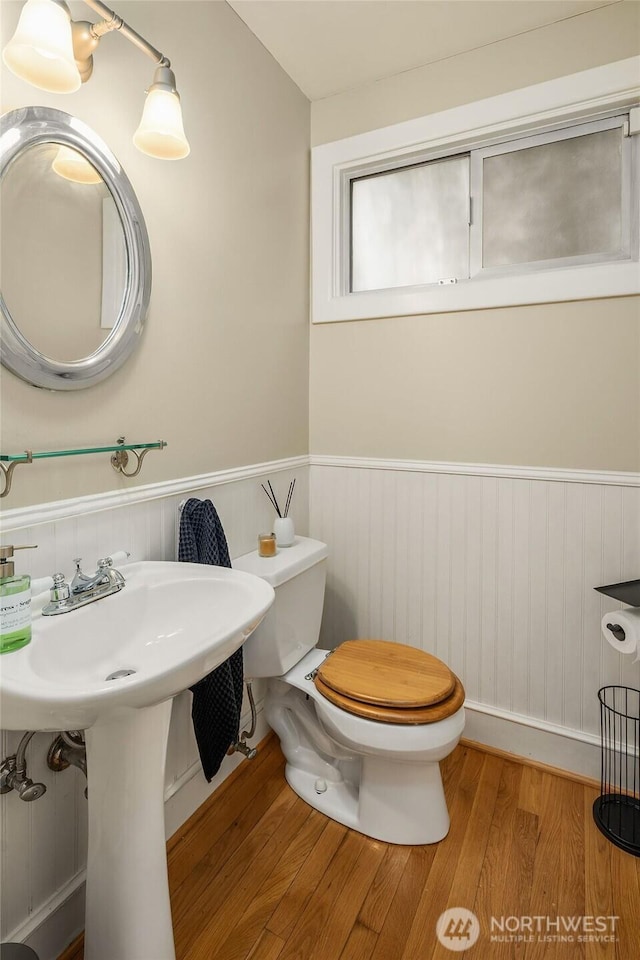 half bathroom with toilet, wood finished floors, and wainscoting