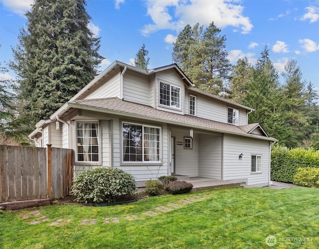 view of front of house with a patio, roof with shingles, a front lawn, and fence