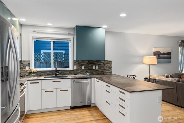 kitchen featuring light wood finished floors, a peninsula, a sink, appliances with stainless steel finishes, and open floor plan