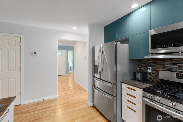 kitchen featuring blue cabinetry, tasteful backsplash, dark countertops, and appliances with stainless steel finishes