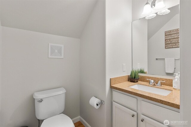 bathroom with baseboards, toilet, vanity, and vaulted ceiling