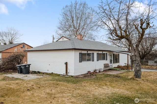 view of side of home featuring a yard, fence, a chimney, and a shingled roof