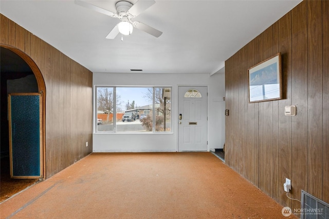 carpeted entryway with visible vents, arched walkways, wooden walls, and a ceiling fan