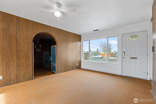 entryway with a ceiling fan, visible vents, arched walkways, wood walls, and carpet flooring