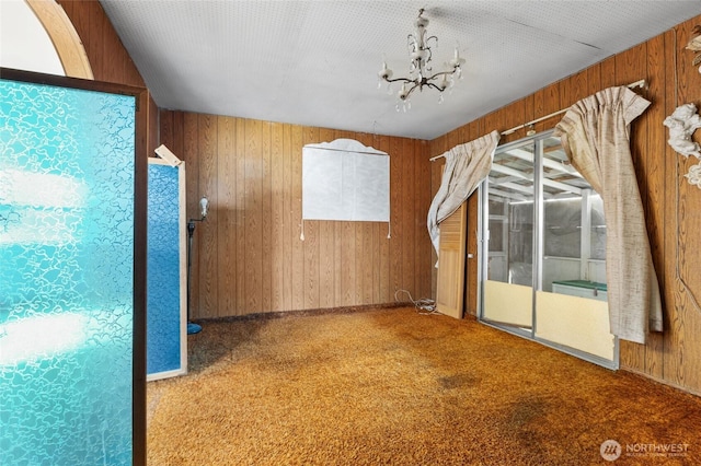 spare room featuring carpet, wood walls, and a chandelier