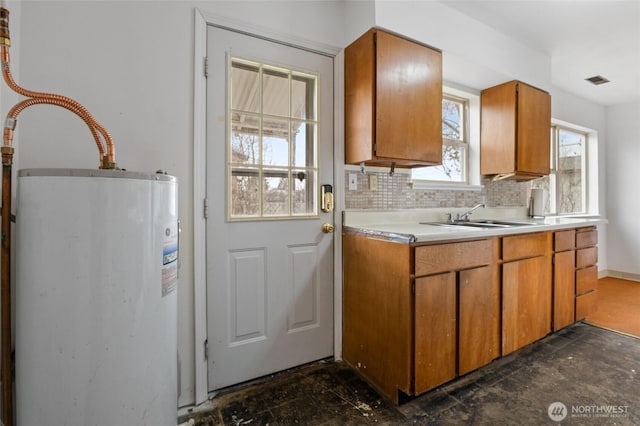 kitchen with backsplash, electric water heater, light countertops, brown cabinetry, and a sink