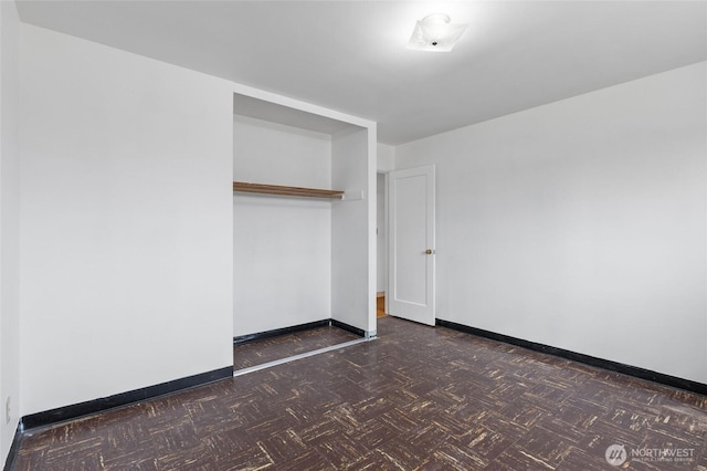 unfurnished bedroom featuring a closet, baseboards, and dark floors