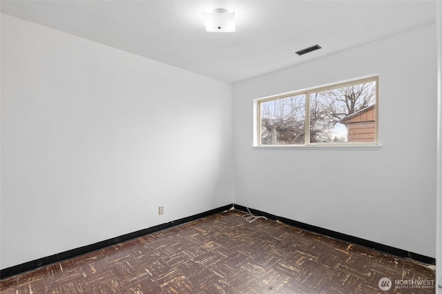 spare room featuring visible vents, baseboards, and dark floors