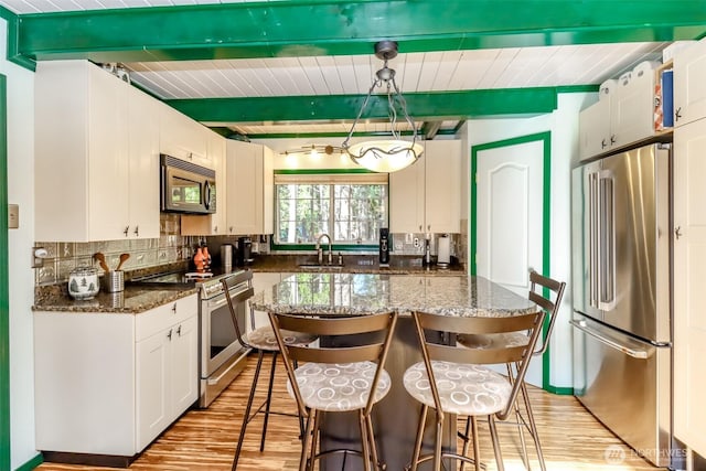 kitchen featuring tasteful backsplash, beamed ceiling, appliances with stainless steel finishes, light wood-style floors, and a sink