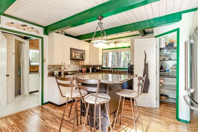 kitchen with light wood finished floors, backsplash, beamed ceiling, stainless steel appliances, and a sink