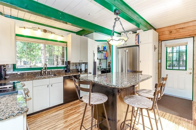 kitchen featuring dishwashing machine, high end fridge, a sink, a kitchen bar, and beamed ceiling