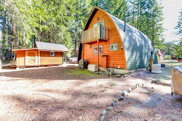 rear view of property featuring a gambrel roof, a storage shed, an outdoor structure, a shingled roof, and a balcony