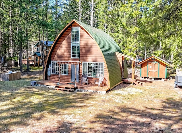 back of property featuring a deck, an outdoor structure, a storage unit, and roof with shingles