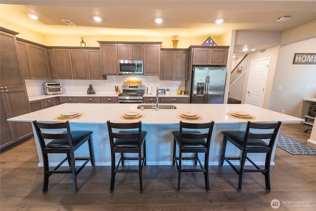 kitchen with a sink, dark wood-type flooring, an island with sink, and stainless steel appliances