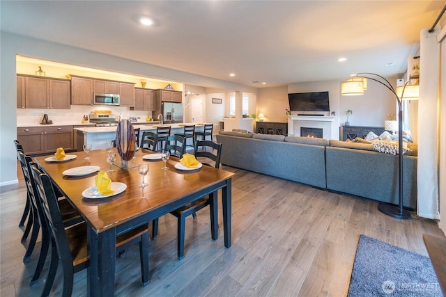 dining space featuring light wood finished floors, recessed lighting, and a warm lit fireplace