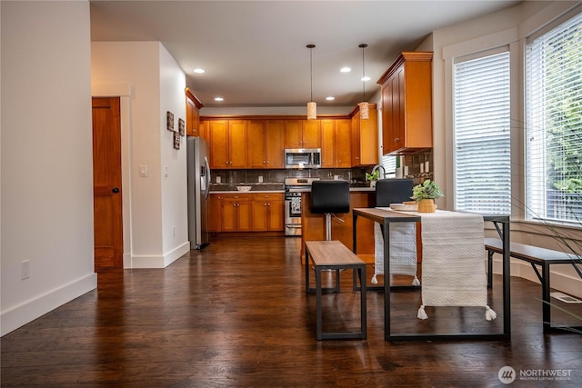 kitchen featuring baseboards, dark wood finished floors, stainless steel appliances, brown cabinets, and backsplash