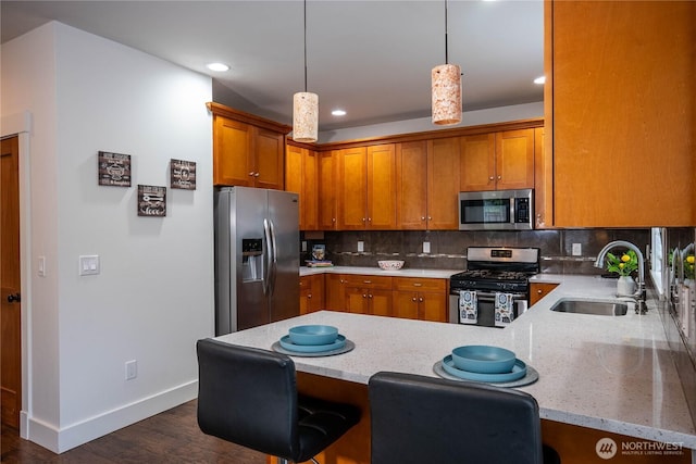 kitchen with a sink, stainless steel appliances, a peninsula, brown cabinetry, and decorative backsplash