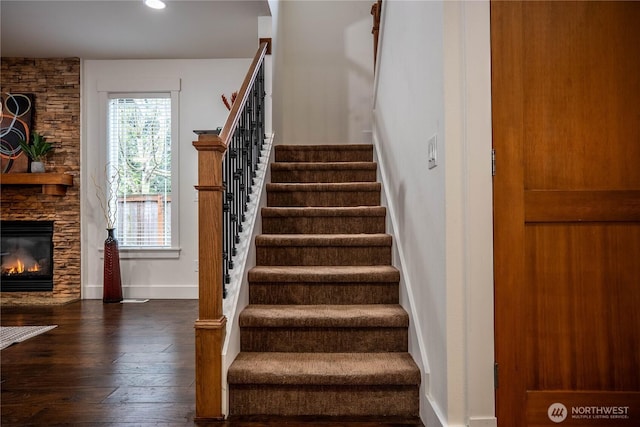 stairway with baseboards, a stone fireplace, and hardwood / wood-style floors