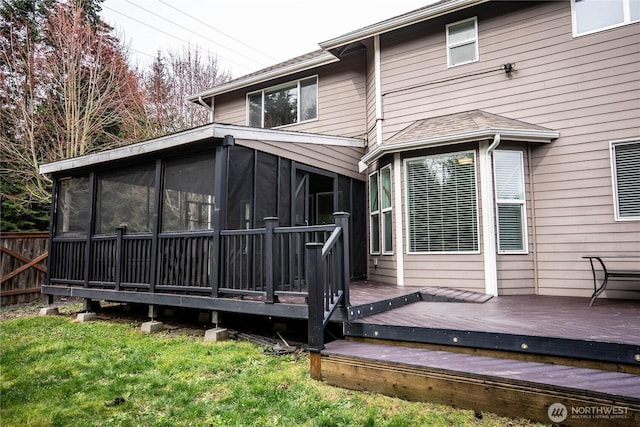 rear view of house featuring fence, a deck, and a sunroom