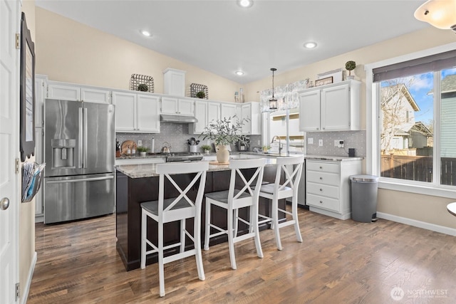 kitchen with under cabinet range hood, a kitchen island, dark wood-style floors, stainless steel fridge, and light countertops