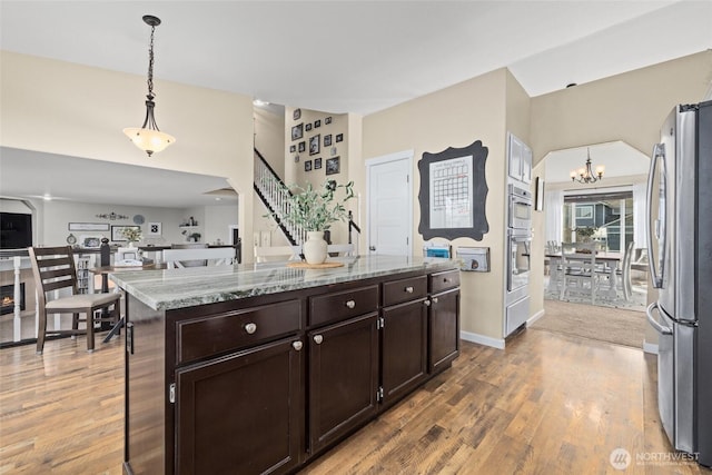 kitchen with light stone counters, appliances with stainless steel finishes, wood finished floors, and an inviting chandelier