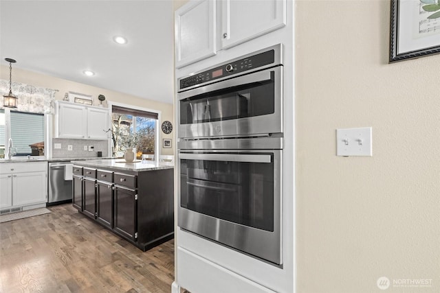 kitchen featuring backsplash, stainless steel appliances, wood finished floors, white cabinetry, and a sink