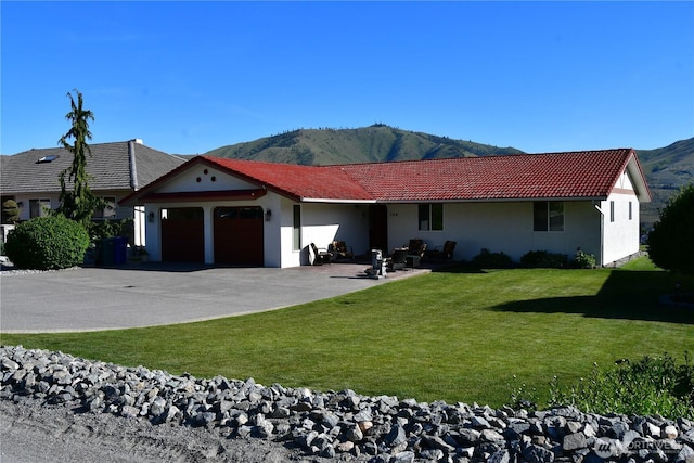 view of front of home with a tiled roof, a front yard, stucco siding, a garage, and a mountain view