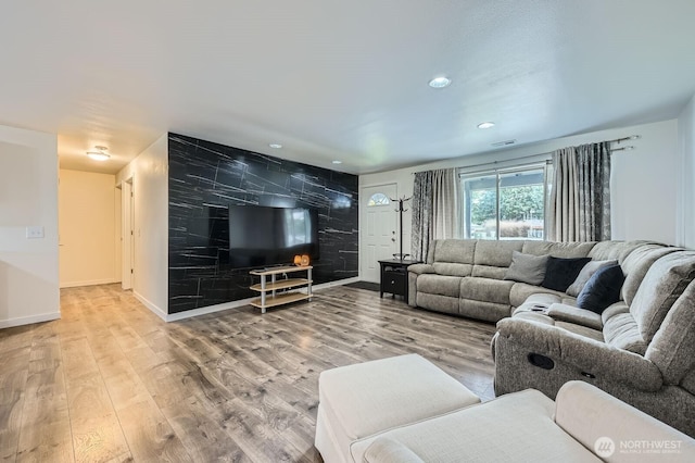 living area featuring visible vents, baseboards, wood finished floors, and an accent wall