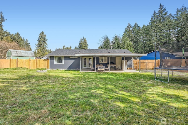 back of property featuring a trampoline, french doors, a fenced backyard, a yard, and a patio