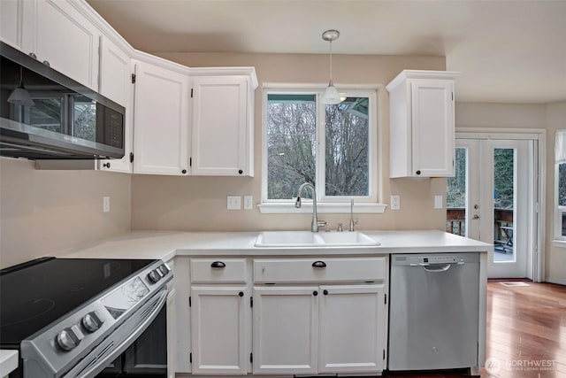 kitchen with light countertops, appliances with stainless steel finishes, wood finished floors, white cabinetry, and a sink