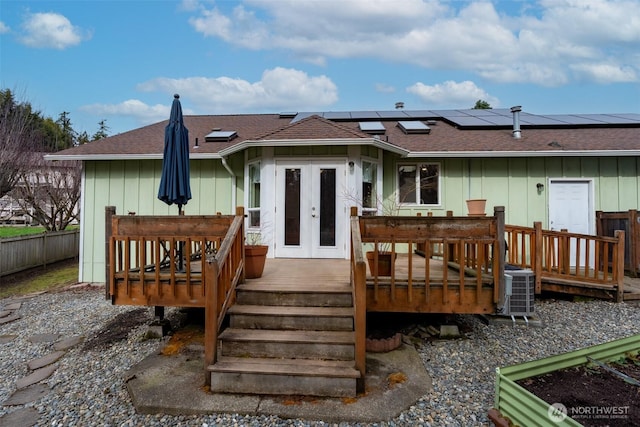 rear view of property with fence, french doors, roof with shingles, a wooden deck, and solar panels