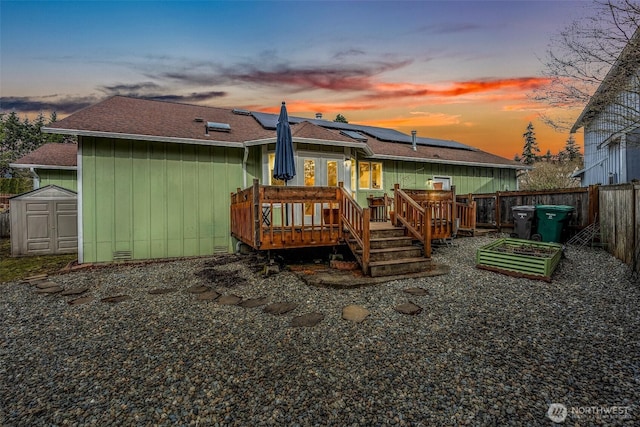 back of property with a shingled roof, an outdoor structure, a storage unit, a deck, and roof mounted solar panels