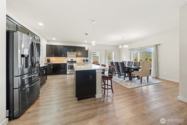 kitchen featuring a sink, stainless steel appliances, light countertops, light wood-style floors, and tasteful backsplash