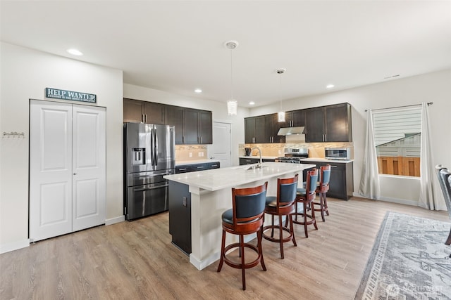 kitchen with under cabinet range hood, stainless steel appliances, a breakfast bar area, light wood finished floors, and light countertops